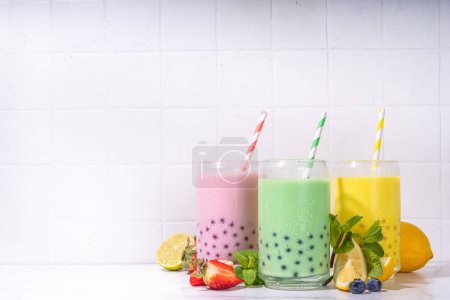 Set of three colorful summer bubble tea, bright creamy pearl tea or latte tapioca drinks, pink berry, yellow citrus, green mint, with tapioca balls and crushed ice, on white background