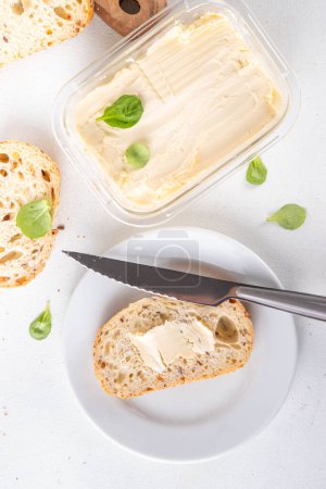Hausgemachte vegane Butter, cremig ohne Milchprodukte, alternative pflanzliche Butter mit Sojabohnenblättern und selbstgebackenes Brot auf weißem Küchentischhintergrund