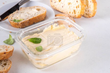 Hausgemachte vegane Butter, cremig ohne Milchprodukte, alternative pflanzliche Butter mit Sojabohnenblättern und selbstgebackenes Brot auf weißem Küchentischhintergrund