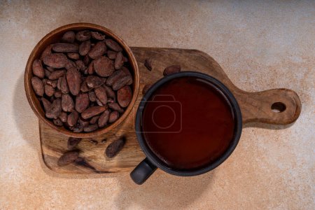 Zeremonielles Kakaotrinken. Heiße Prunkschokolade in schwarzer Tasse mit Kakaobohnen. Frauenhände halten Kakaotasse. Gesundes Bio-Schokoladengetränk aus Bohnen, ohne Sahne, Zucker oder Toppings