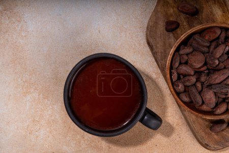 Bebida ceremonial de cacao. Chocolate ceremonial caliente en taza negra con granos de cacao. Manos de mujer sosteniendo taza de cacao. Bebida orgánica saludable de chocolate preparada a partir de frijoles, sin crema, azúcar ni aderezos