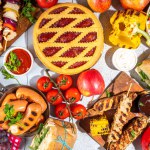 Various picnic barbeque food and drink flatlay. Summer bbq picnic food, assorted grilled meats, kebabs, vegetable, fruit salad, traditional picnic summer pie cake, sandwiches, top view copy space