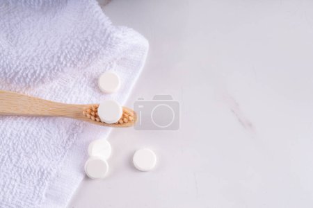 Toothpaste pills tablets on toothbrush, white solid toothpaste tablet with bamboo toothbrush on modern white bathroom background