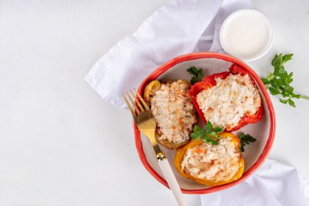 Stuffed bell peppers on white kitchen table background. Colorful red, yellow, green peppers with diet chicken minced meat, vegetables and rice, with white sauce, Balanced healthy food recipe