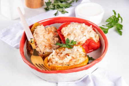 Photo for Stuffed bell peppers on white kitchen table background. Colorful red, yellow, green peppers with diet chicken minced meat, vegetables and rice, with white sauce, Balanced healthy food recipe - Royalty Free Image