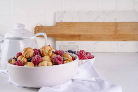 Winzige Frühstückscroissants Müsli mit frischen Beeren und Milch. Schüsselportionen mit trendigen frisch gebackenen Mini-Croissants mit Himbeere und Blaubeere, Dessert-Snack am Morgen