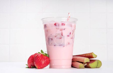 Strawberry rhubarb milkshake, frozen creamy cocktail drink with whipped ice cream, rhubarb and sliced strawberries copy space