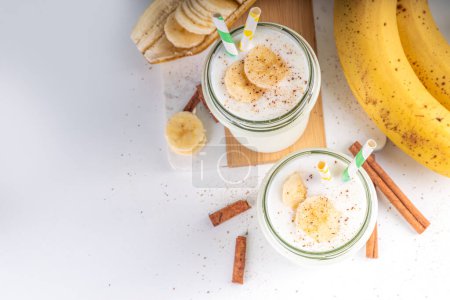 Téléchargez les photos : Smoothie aux bananes, shake ou yaourt à la cannelle végétalien d'automne dans un bocal en verre sur fond clair. Aliments sains - en image libre de droit