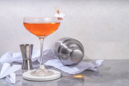 Cocktail alcoolisé alcoolisé alcoolisé bourbon, whisky, amaro, apéritif apéro, jus de citron frais et papier avion décor artisanal, sur fond blanc avec lumière dure et ustensiles de bar