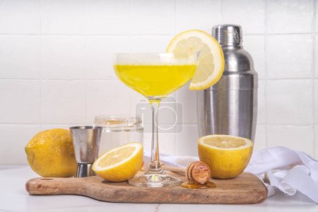 Süß-saurer alkoholischer Bienenknies-Cocktail. Hausgemachte Zitrus-Honigbienen Knie trinken mit Zutaten, auf weißem Hintergrund mit hartem Licht und Bar-Utensilien