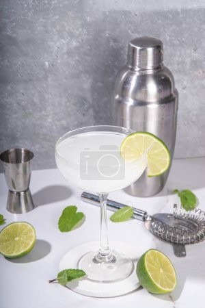 Gimlet cocktail d'alcool d'agrumes. Boisson alcoolisée aigre-douce, avec gin ou vodka et garniture de lime, sur gris clair avec ustensiles de bar et lumière dure