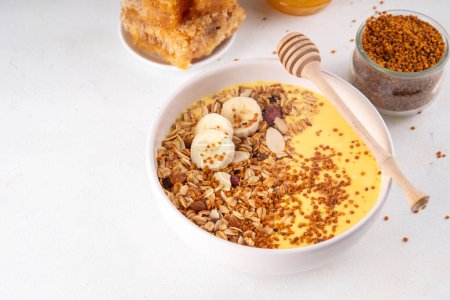 Healthy superfood fruit smoothie bowl with bee pollen, golden creamy shake or smoothie, with granola and banana. Clean eating, dieting vegetarian dish with bee pollen superfood organic powder 