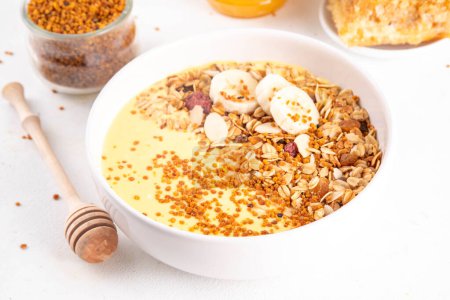 Healthy superfood fruit smoothie bowl with bee pollen, golden creamy shake or smoothie, with granola and banana. Clean eating, dieting vegetarian dish with bee pollen superfood organic powder 