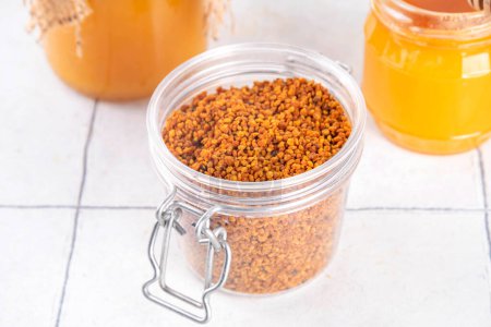 Bee pollen jar and spoon with honey and honeycomb. Trendy superfood, antioxidant organic powder, on white table background copy space