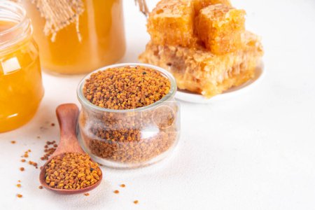Bee pollen jar and spoon with honey and honeycomb. Trendy superfood, antioxidant organic powder, on white table background copy space