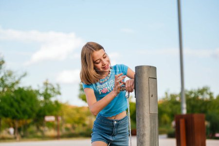 Téléchargez les photos : La fille très heureuse buvant de l'eau à la fontaine dans un parc municipal. - en image libre de droit