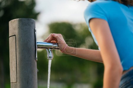 Foto de La chica muy feliz bebiendo agua en la fuente en un parque de la ciudad. - Imagen libre de derechos
