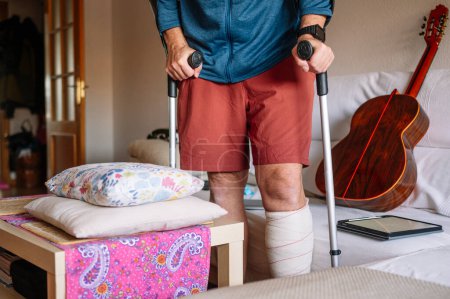 Téléchargez les photos : Homme blessé avec un pied bandé marchant à la maison avec des bâtons de marche. - en image libre de droit