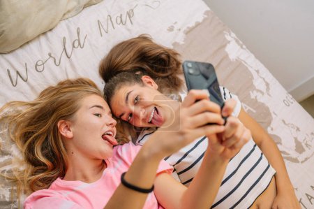 Téléchargez les photos : Deux jeunes filles qui prennent des selfies dans leur chambre. - en image libre de droit