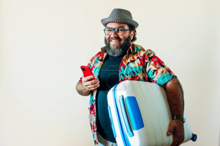 Foto de Hombre gordo barbudo usando un teléfono inteligente y llevando una maleta para viajar. - Imagen libre de derechos