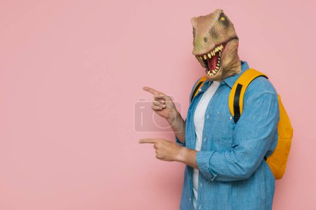 Foto de Hombre con mochila y máscara de lagarto sobre fondo rosa. - Imagen libre de derechos