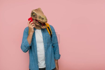 Photo for Man with backpack and lizard mask over pink background using phone. - Royalty Free Image