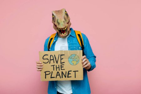 Foto de Hombre con mochila y máscara de lagarto sobre fondo rosa sostiene signo para salvar el planeta. - Imagen libre de derechos