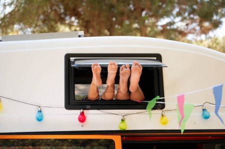 Foto de Los pies de los niños sobresalen por la ventana de la furgoneta en un maravilloso día de acampada. Concepto Vanlife. - Imagen libre de derechos