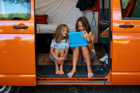 Foto de Dos hermanos usando la tableta en un maravilloso día acampando en una furgoneta. Concepto Vanlife. - Imagen libre de derechos