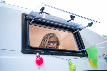 Foto de El chico feliz saca la cabeza por la ventana de la furgoneta en un día maravilloso en el campamento. Concepto Van Life. - Imagen libre de derechos