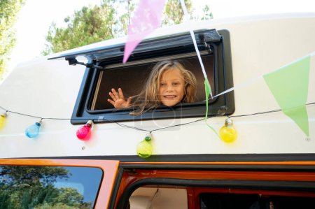 Téléchargez les photos : Happy boy sort la tête par la fenêtre du van lors d'une merveilleuse journée au camp. Concept de vie Van. - en image libre de droit