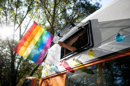 Téléchargez les photos : Main tenant un drapeau de fierté par la fenêtre d'un camping-car. - en image libre de droit