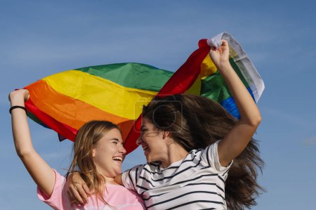 Foto de Dos novias besando y ondeando la bandera del orgullo LGBT. - Imagen libre de derechos