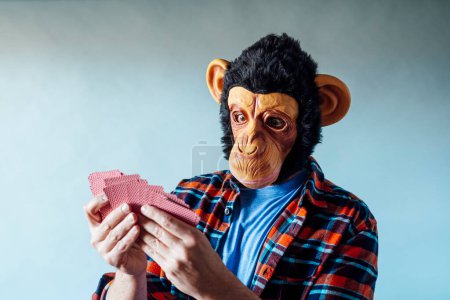 Foto de Hombre con máscara de mono y la celebración de póquer jugando a las cartas sobre fondo azul. - Imagen libre de derechos