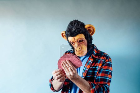 Téléchargez les photos : Homme portant un masque de singe et tenant des cartes à jouer au poker sur fond bleu. - en image libre de droit