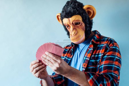 Photo for Man wearing monkey mask and holding poker playing cards on blue background. - Royalty Free Image