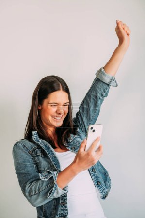Foto de Mujer eufórica mirando su teléfono inteligente y levantando el brazo. - Imagen libre de derechos