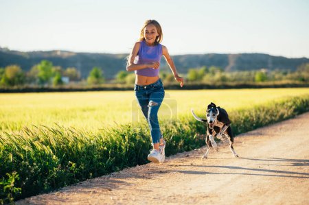 Foto de Hermosa joven rubia corriendo en el campo con su perro galgo. - Imagen libre de derechos