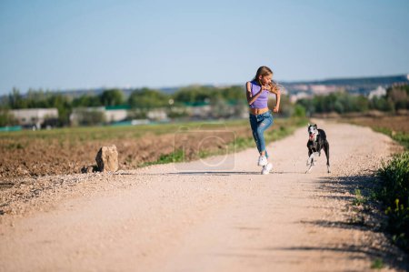 Téléchargez les photos : Belle jeune femme blonde courant sur le terrain avec son chien lévrier. - en image libre de droit