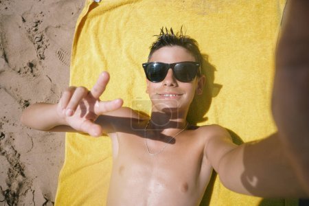 Téléchargez les photos : Adolescent couché sur la serviette lors d'une journée fabuleuse à la plage. - en image libre de droit