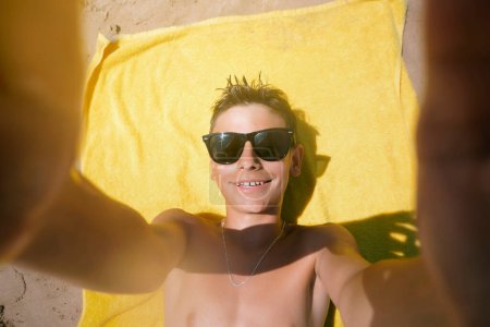 Téléchargez les photos : Adolescent couché sur la serviette lors d'une journée fabuleuse à la plage. - en image libre de droit
