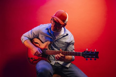Photo for Man playing electric guitar on red background - Royalty Free Image