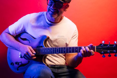 Téléchargez les photos : Homme jouant de la guitare électrique sur fond rouge - en image libre de droit