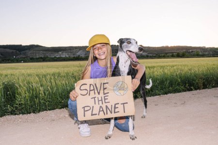 Photo for Beautiful teenager holding a sign that says SAVE THE PLANET next to her dog. - Royalty Free Image