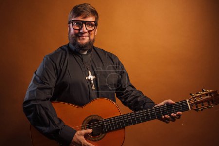 Téléchargez les photos : Portrait d'un prêtre avec un crucifix et chemise noire jouant de la guitare. - en image libre de droit
