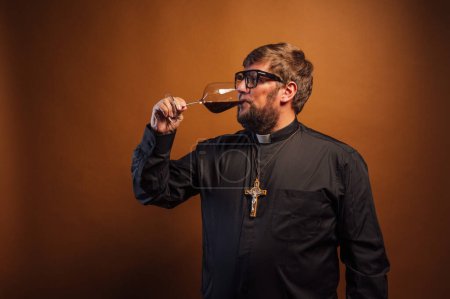 Téléchargez les photos : Portrait d'un prêtre avec crucifix et lunettes de soleil buvant du vin. - en image libre de droit