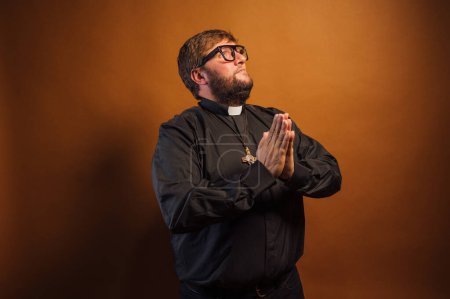 Téléchargez les photos : Portrait d'un prêtre avec crucifix et chemise noire priant. - en image libre de droit