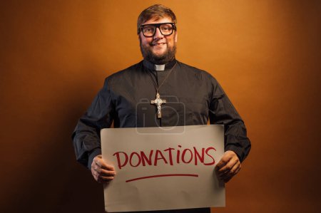 Téléchargez les photos : Portrait d'un prêtre avec crucifix et chemise noire demandant des dons d'argent pour l'église avec un signe. - en image libre de droit