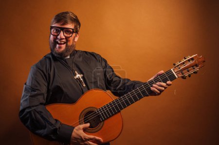 Photo for Portrait of a priest with a crucifix and black shirt playing the guitar. - Royalty Free Image