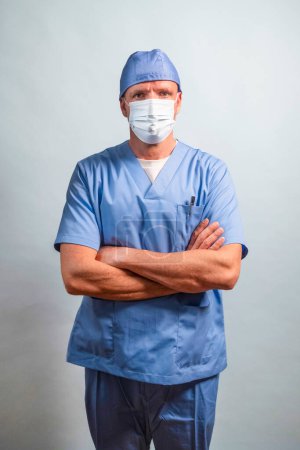 Foto de Retrato de un médico vestido de azul claro, máscara y gorra mirando a la cámara en el estudio. - Imagen libre de derechos